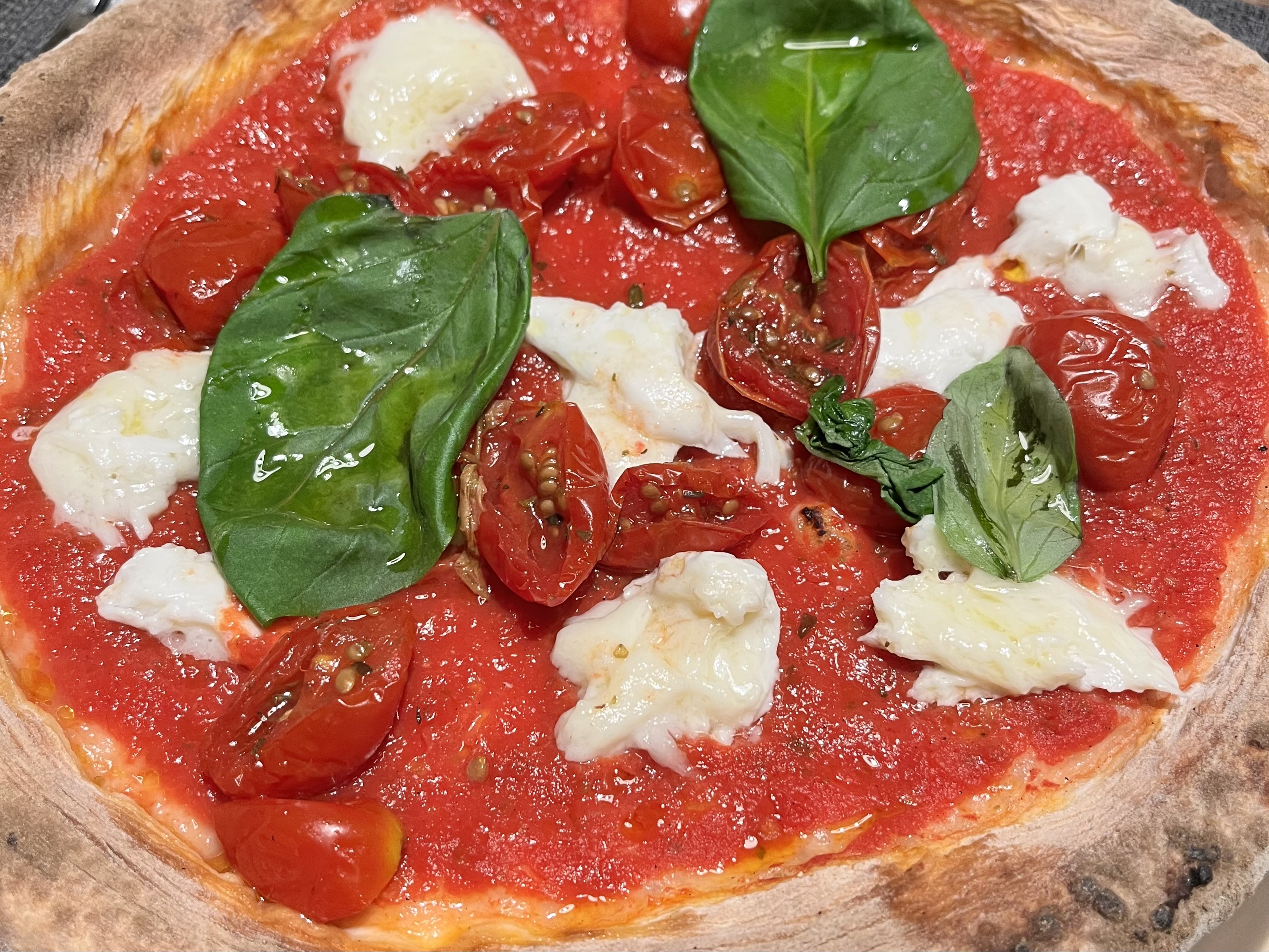 A close-up of a pizza with tomato sauce, cherry tomatoes, basil, and buffalo mozzarella.